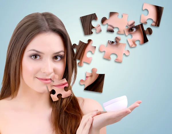 Beautiful girl with cream with parts of skin on puzzles on blue background — Stock Photo, Image