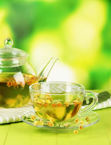 Wasserkocher und Tasse Tee mit Linde auf Holztisch auf Naturhintergrund — Stockfoto