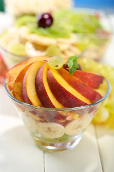 Salada de frutas saborosas em tigelas de vidro, em mesa de madeira branca — Fotografia de Stock