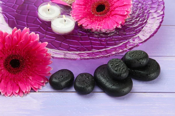 Pedras de spa, belas flores de gerbera e velas na água — Fotografia de Stock