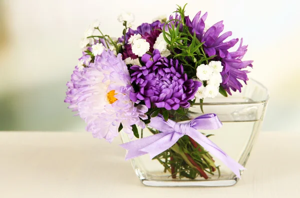 Beautiful bouquet of bright flowers in glass vase, on wooden table, on bright background — Stock Photo, Image