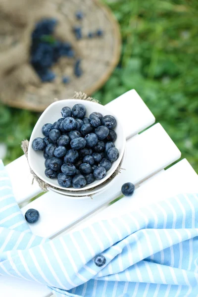 Blueberries in plates near napkin on wooden table on grass background — Stock Photo, Image