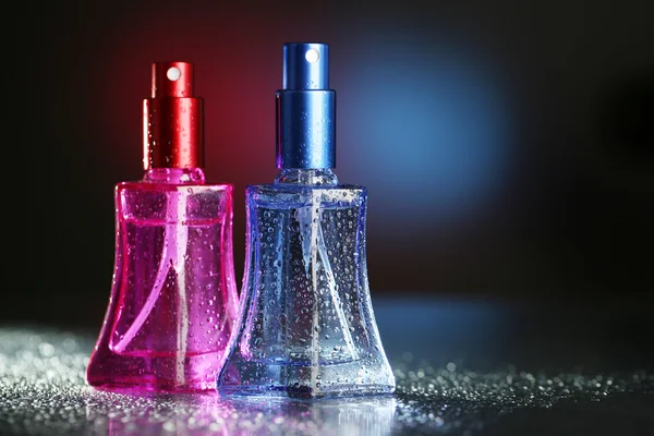 Perfume de las mujeres en hermosas botellas sobre fondo oscuro con luz de color —  Fotos de Stock
