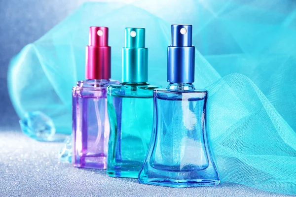 Perfume de mujer en hermosas botellas sobre fondo azul —  Fotos de Stock