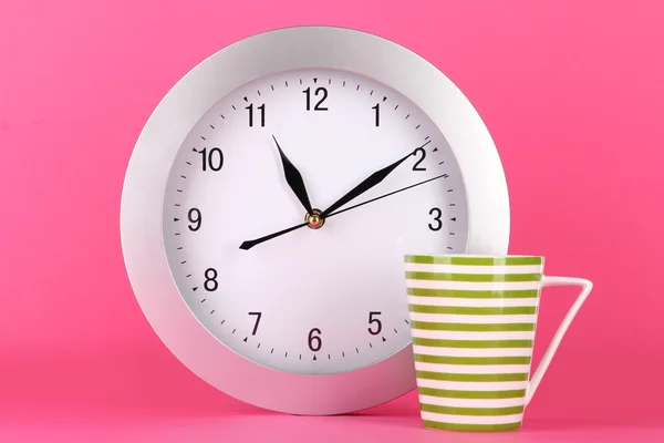 Šálek čaje a hodiny na růžovém pozadí — Stock fotografie