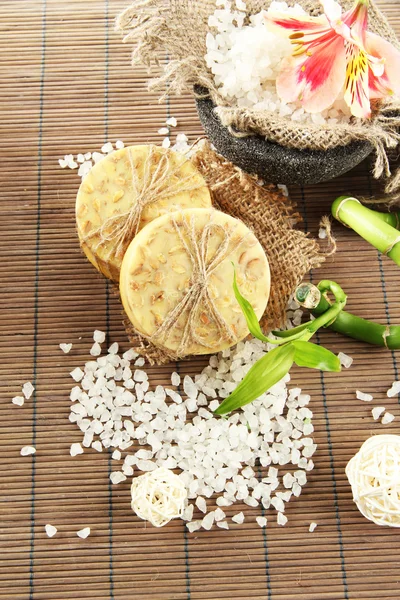 Hand-made soap and sea salt on grey bamboo mat — Stock Photo, Image