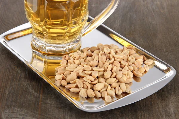 Cerveza en vaso y nueces en bandeja sobre mesa de madera —  Fotos de Stock