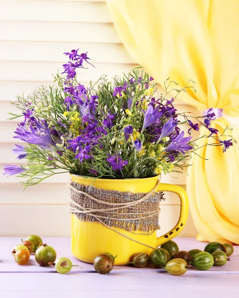 Hermoso ramo de flores silvestres en taza y bayas en mesa de madera — Foto de Stock