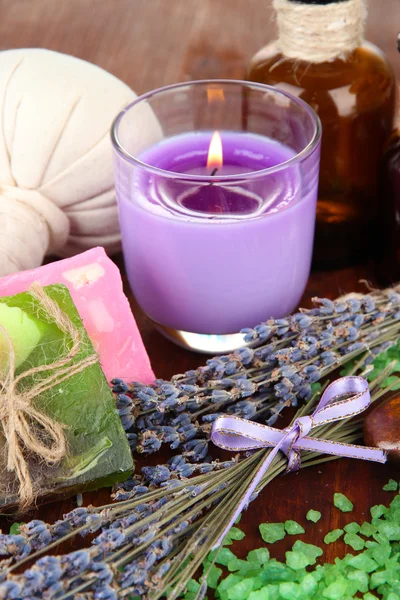Asetelma laventeli kynttilä, saippua, hieronta pallot, pullot, saippua ja tuore laventeli, puinen pöytä taustalla — kuvapankkivalokuva