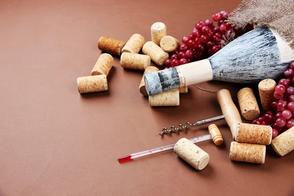 Vieja botella de vino, uvas y corchos sobre fondo marrón —  Fotos de Stock
