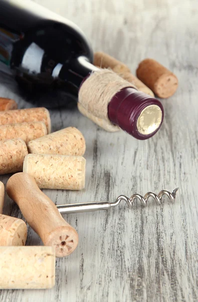 Corkscrew with wine corks and bottle of wine on wooden table close-up — Stock Photo, Image