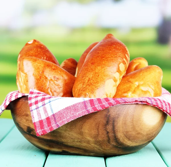 Fresh baked pasties, in wooden bowl, on wooden table, on bright background — Stock Photo, Image