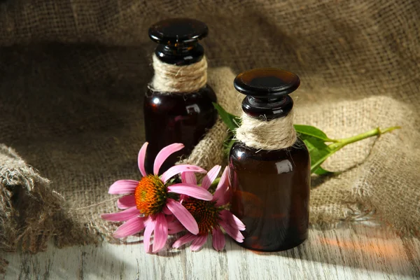Medicine bottles with purple echinacea flowers on wooden table with burlap — Stock Photo, Image