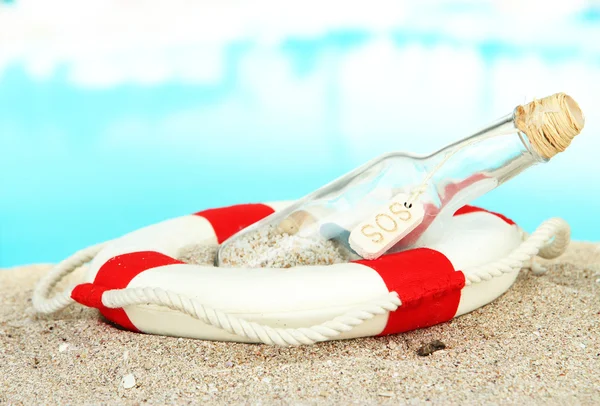 Glas flaska med meddelande inne om sand, på ljusa blå bakgrund — Stockfoto