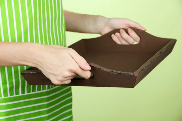 Woman in green apron holding wooden tray, on color background — Stock Photo, Image