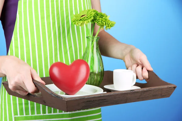 Žena v zelené zástěře drží dřevěný tác se snídaní, na barvu pozadí — Stock fotografie