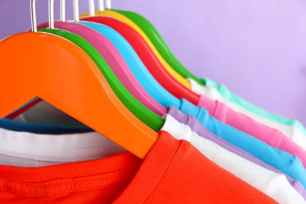 Verschillende shirts op kleurrijke hangers op paarse achtergrond — Stockfoto