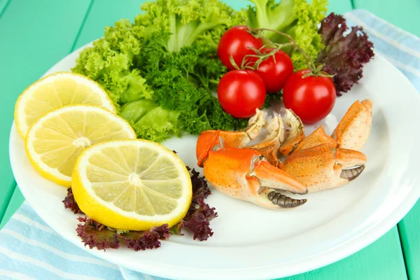 Pinces de crabe bouillies sur plaque blanche avec feuilles de salade et tomates, sur fond de table en bois — Photo
