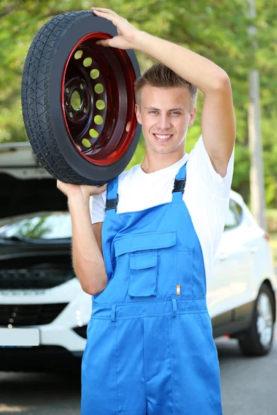 Auto mechanic with tire on his shoulder — Stock Photo, Image