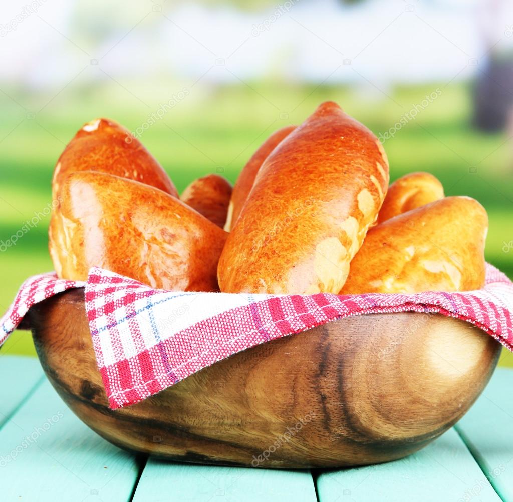 Fresh baked pasties, in wooden bowl, on wooden table, on bright background