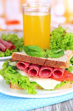 Lezzetli sandviç salam sosis ve ahşap masa arka plan üzerinde renkli peçete üzerinde sebze ve meyve suyu ile kompozisyon