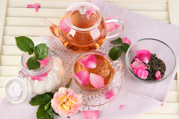 Kettle and cup of tea from tea rose on napkin on wooden background — Stock Photo, Image