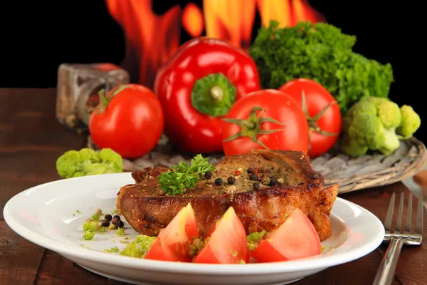 Кусок жареного мяса на тарелке на деревянном столе на огненном фоне — стоковое фото