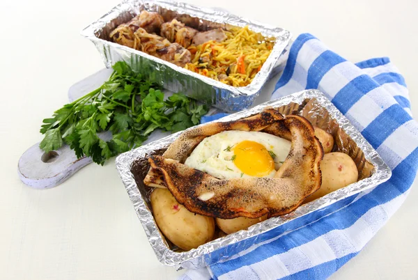 Food in boxes of foil on napkin on wooden board isolated in white