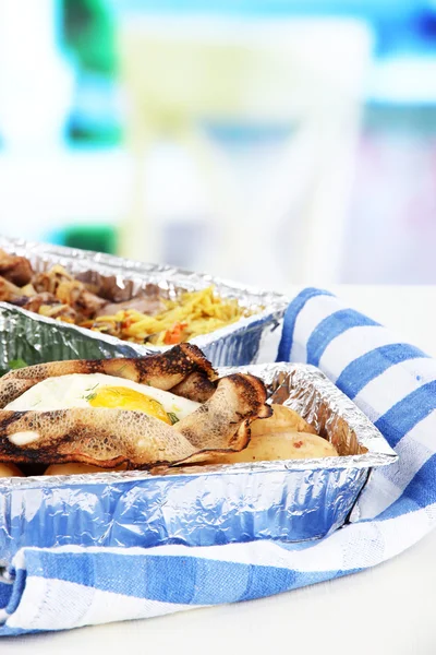 Food in boxes of foil on napkin on wooden board on room background — Stock Photo, Image