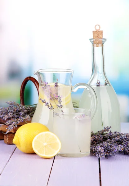 Limonata di lavanda in bottiglia di vetro e brocca, su tavolo di legno viola, su sfondo brillante — Foto Stock