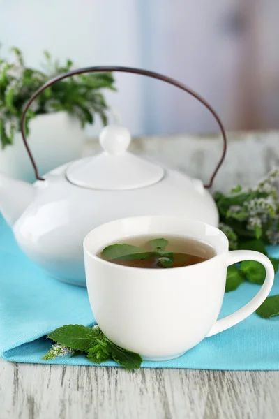 Tetera y taza de té de hierbas con flores de menta fresca en la mesa de madera —  Fotos de Stock