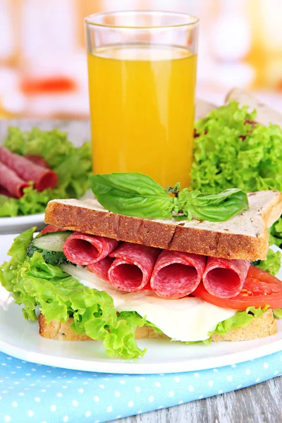 Composição com suco de frutas e saboroso sanduíche com salsicha de salame e legumes em guardanapo de cor, em fundo de mesa de madeira — Fotografia de Stock