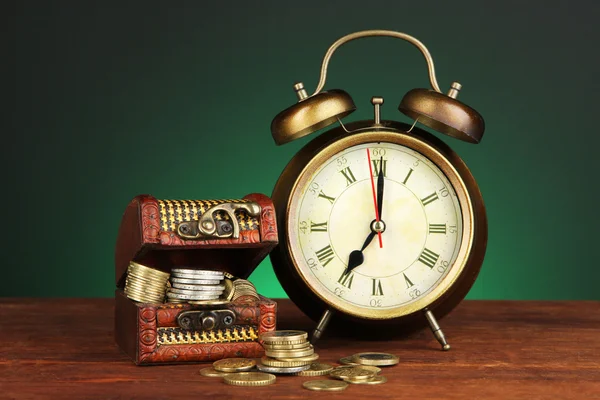 Horloge antique et pièces de monnaie sur table en bois sur fond de couleur sombre — Photo