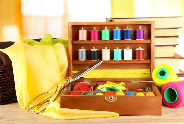 Sewing kit in wooden box with books and cloth table on bright background — Stock Photo, Image