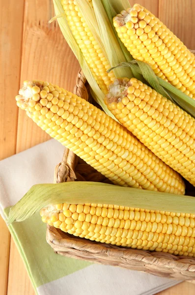 Crude corns in basket on napkin on wooden table — Stock Photo, Image