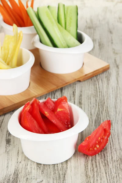 Bright fresh vegetables cut up slices in bowls on wooden table close-up