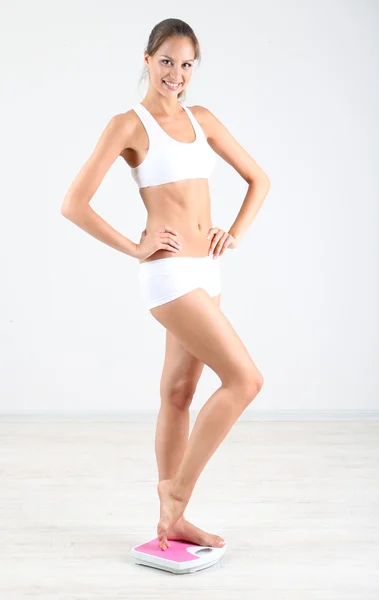 Slim young girl on scales on gray background — Stock Photo, Image