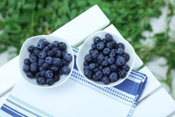 Blueberries in plates on napkin on wooden table on grass background — Stock Photo, Image