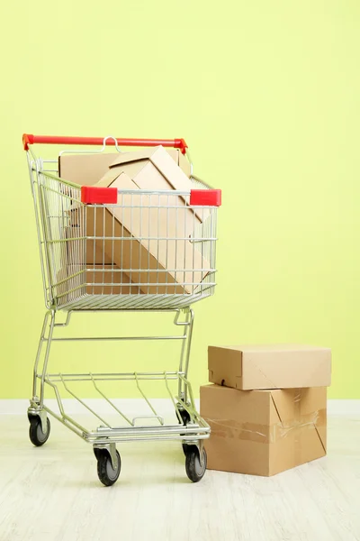 Shopping cart with carton, on green wall background — Stock Photo, Image