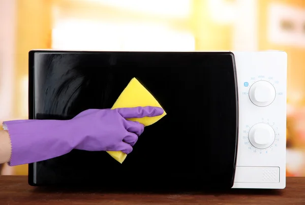 Hand with sponge cleaning microwave oven, on bright background — Stock Photo, Image