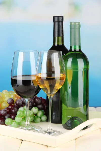 Wine bottles and glasses of wine on tray, on bright background — Stock Photo, Image