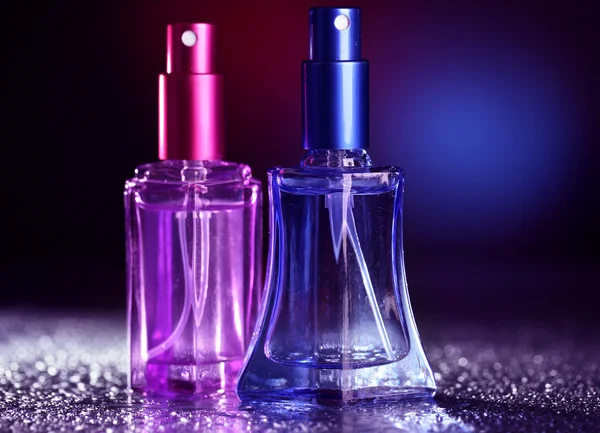 Women perfume in beautiful bottles on dark background with color light — Stock Photo, Image