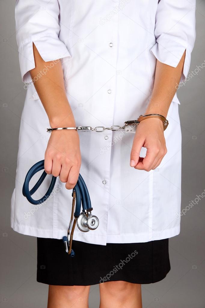 Doctor with syringestethoscope in handcuffs on grey background