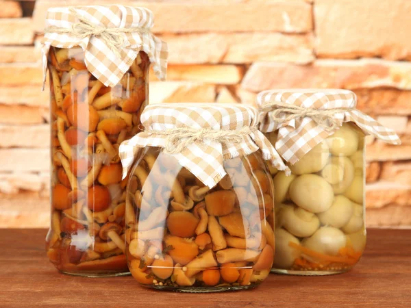 Delicious marinated mushrooms in glass jars, on wooden table on bright background — Stock Photo, Image