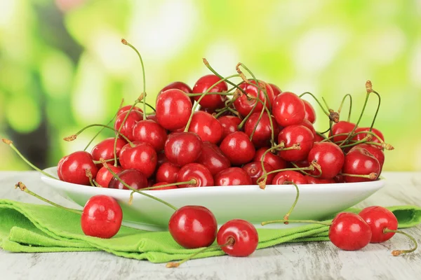 Kirschbeeren auf Teller auf Holztisch auf hellem Hintergrund — Stockfoto