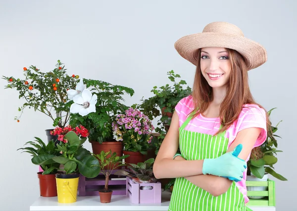 Garota bonita jardineiro com flores no fundo cinza — Fotografia de Stock