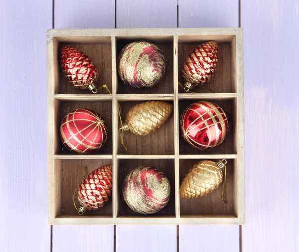 Holzkiste gefüllt mit Weihnachtsschmuck, auf farbigem Holzgrund — Stockfoto