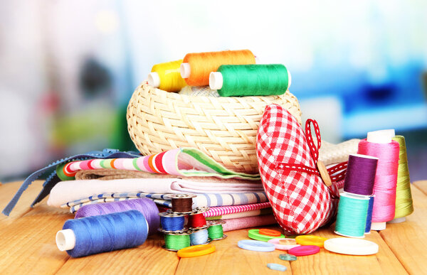 Плетеная корзина с аксессуарами для рукоделия на деревянном столе, на ярком фоне
