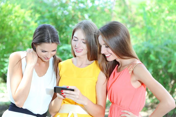 Three beautiful young woman with smartphone in summer park — Stock Photo, Image