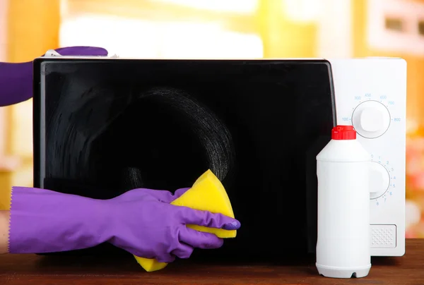 Ręka z gąbki do czyszczenia kuchenka mikrofalowa, na jasnym tle — Zdjęcie stockowe